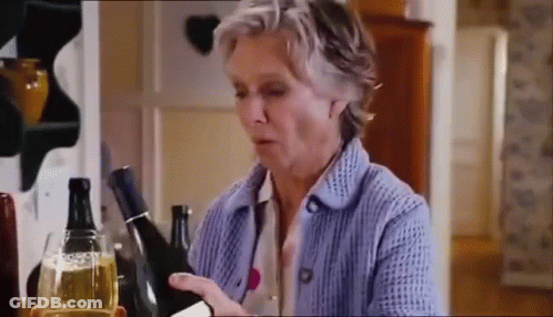 A Woman In A Blue Sweater Is Holding A Bottle Of Wine And A Glass Of Wine . GIF