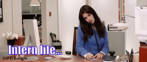 A Woman In A Blue Sweater Is Sitting At A Desk In Front Of A Computer With The Words Intern Life Written Above Her GIF