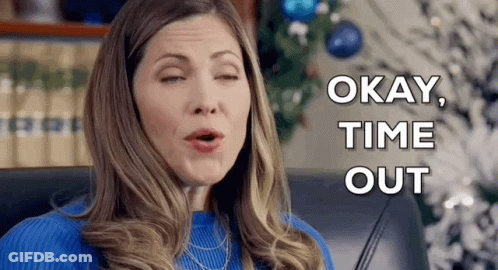 A Woman In A Blue Sweater Is Sitting In Front Of A Christmas Tree And Making A Face . GIF