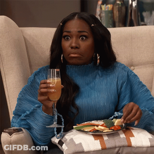 A Woman In A Blue Sweater Is Sitting On A Couch Holding A Glass Of Wine And A Plate Of Food GIF