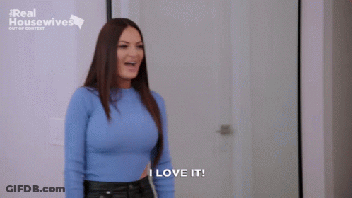 A Woman In A Blue Sweater Is Standing In Front Of A Door And Says I Love It . GIF