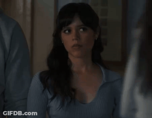 A Woman In A Blue Sweater Is Standing Next To A Man And Looking At The Camera . GIF