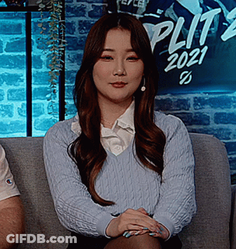 A Woman In A Blue Sweater Sits On A Couch In Front Of A Split 2021 Sign GIF