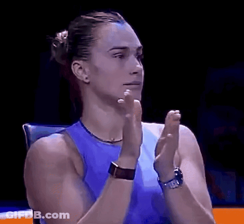 A Woman In A Blue Tank Top Is Clapping Her Hands In A Dark Room . GIF