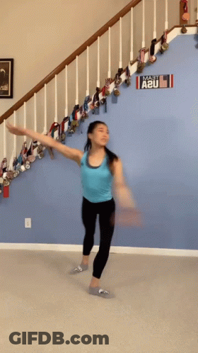 A Woman In A Blue Tank Top Is Dancing In Front Of A Sign That Says A2u GIF