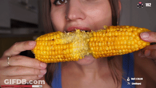 A Woman In A Blue Tank Top Is Eating Corn On The Cob With 162 In The Corner GIF