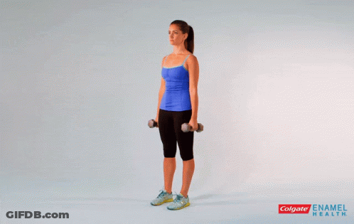 A Woman In A Blue Tank Top Is Holding Dumbbells Over Her Shoulder GIF