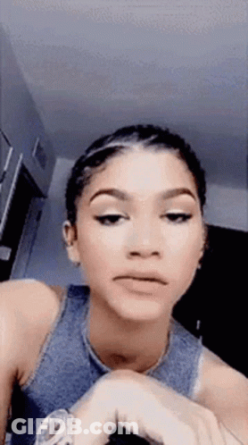 A Woman In A Blue Tank Top Is Making A Funny Face While Looking At Her Watch . GIF