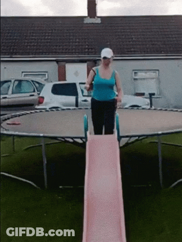 A Woman In A Blue Tank Top Is On A Pink Slide On A Trampoline GIF