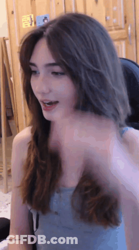 A Woman In A Blue Tank Top Is Sitting In Front Of A Wooden Door GIF