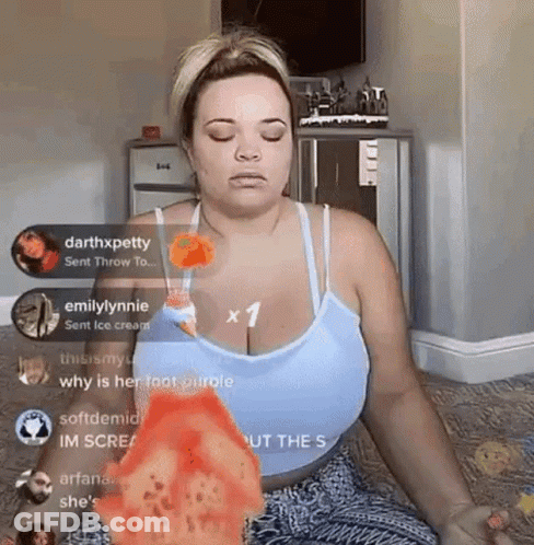 A Woman In A Blue Tank Top Is Sitting On The Floor With Her Eyes Closed And Holding A Slice Of Pizza . GIF