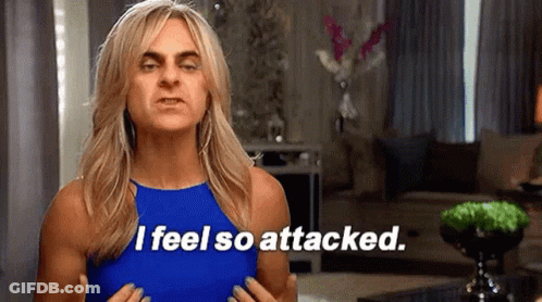 A Woman In A Blue Tank Top Is Standing In A Living Room And Saying `` I Feel So Attacked . '' GIF