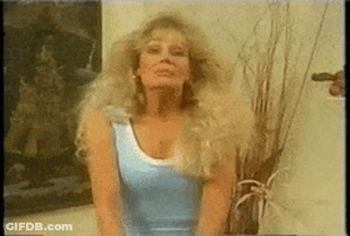 A Woman In A Blue Tank Top Stands In Front Of A Plant GIF
