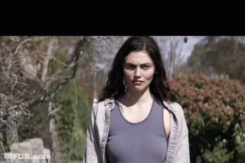 A Woman In A Blue Tank Top Stands In Front Of Bushes GIF