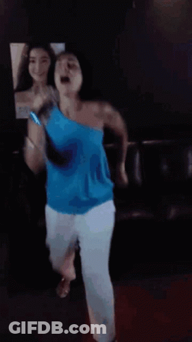 A Woman In A Blue Top Is Dancing In Front Of A Mirror GIF