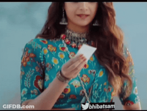 A Woman In A Blue Top Is Holding A Piece Of Paper With The Twitter Hashtag Bhibatsam Visible GIF