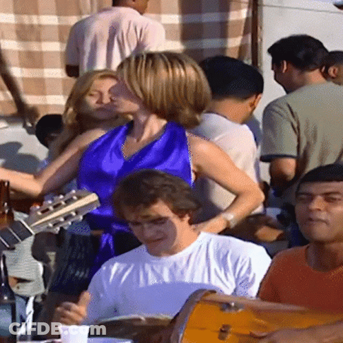 A Woman In A Blue Top Is Playing A Guitar While A Man Plays Drums GIF