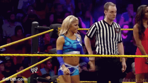 A Woman In A Blue Top Is Standing In A Wrestling Ring Next To A Referee Wearing A Black And White Striped Shirt GIF