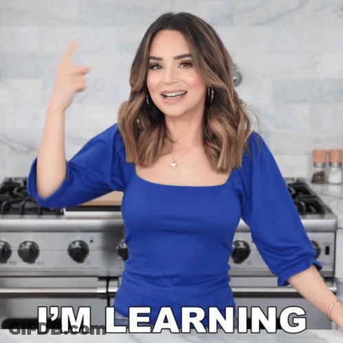 A Woman In A Blue Top Is Standing In Front Of A Stove And Says I 'M Learning GIF