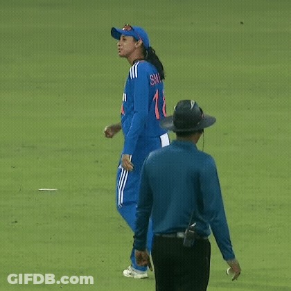 A Woman In A Blue Uniform Is Walking On A Cricket Field Next To A Referee . GIF