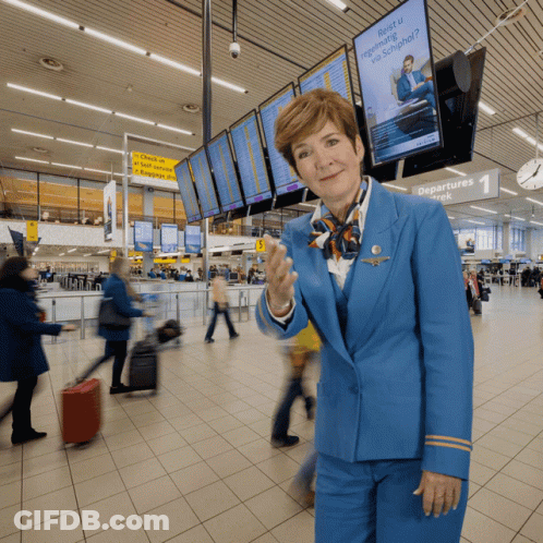 A Woman In A Blue Uniform Stands In Front Of A Sign That Says Departures Week GIF
