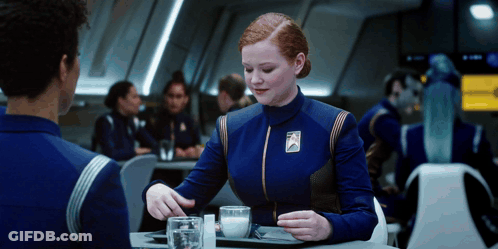 A Woman In A Blue Uniform With A Badge That Says ' Star Trek ' On It GIF