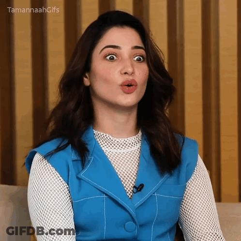 A Woman In A Blue Vest And White Shirt Is Making A Funny Face . GIF