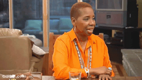 A Woman In A Bright Orange Shirt Is Sitting At A Table With A Glass Of Water . GIF