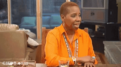 A Woman In A Bright Orange Shirt Is Sitting At A Table With A Glass Of Water . GIF