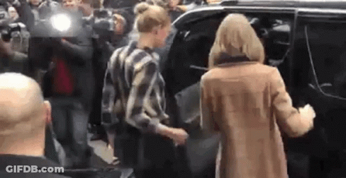 A Woman In A Brown Coat Is Getting Out Of A Car In Front Of A Crowd Of People . GIF