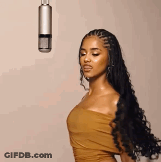 A Woman In A Brown Dress Is Standing In Front Of A Microphone . GIF