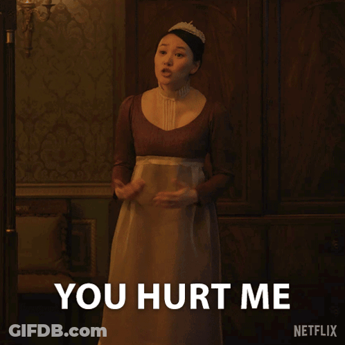 A Woman In A Brown Dress Is Standing In Front Of A Sign That Says You Hurt Me GIF