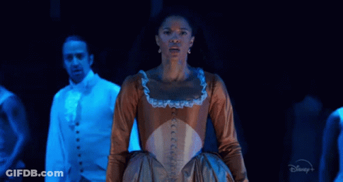 A Woman In A Brown Dress Is Standing On A Stage In Front Of A Man In A Blue Suit . GIF