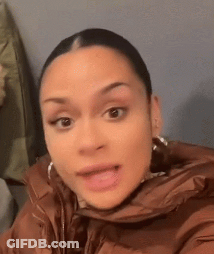 A Woman In A Brown Jacket And Earrings Is Making A Funny Face . GIF