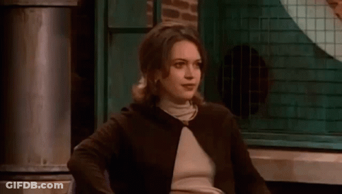 A Woman In A Brown Jacket And Turtleneck Is Sitting In A Chair In Front Of A Window . GIF