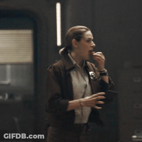 A Woman In A Brown Jacket Is Eating Something While A Man Looks On GIF