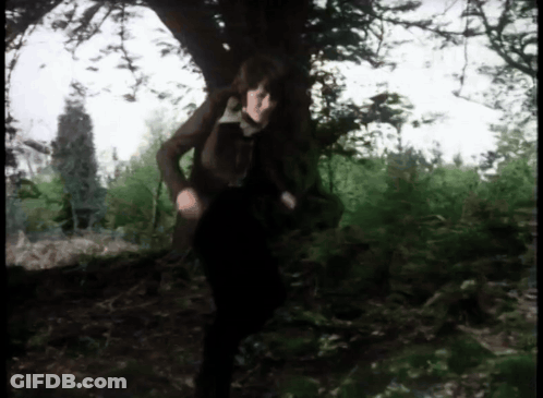 A Woman In A Brown Jacket Is Standing Under A Tree GIF