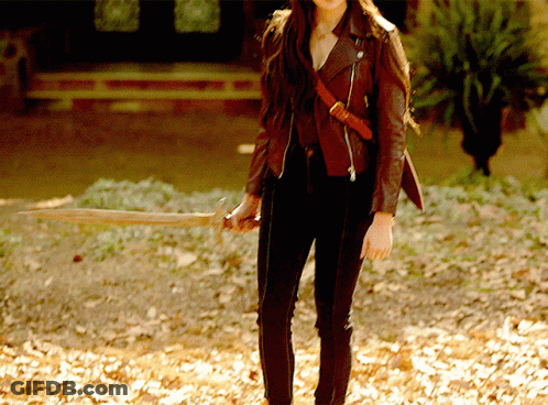 A Woman In A Brown Leather Jacket Holds A Wooden Stick GIF