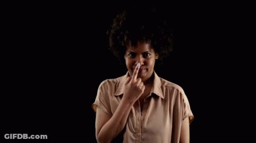 A Woman In A Brown Shirt Holds Her Finger To Her Nose Against A Black Background GIF