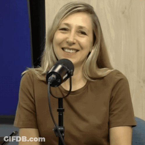 A Woman In A Brown Shirt Is Smiling In Front Of A Black Microphone GIF