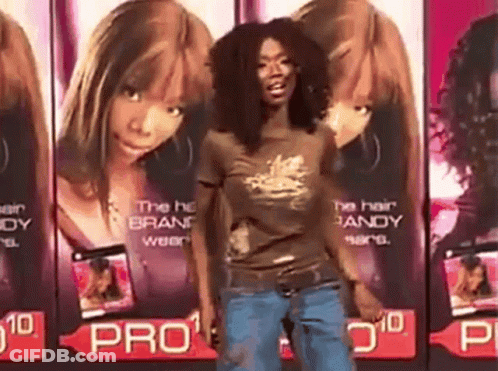 A Woman In A Brown Shirt Is Standing In Front Of A Row Of Advertisements For Pro GIF