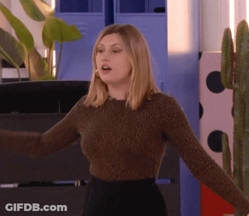 A Woman In A Brown Sweater Is Standing In Front Of A Cactus GIF