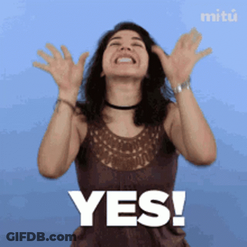 A Woman In A Brown Tank Top Says Yes With Her Hands In The Air GIF