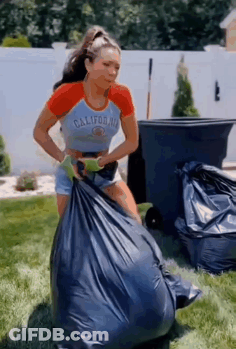 A Woman In A California Shirt Is Holding A Large Garbage Bag . GIF