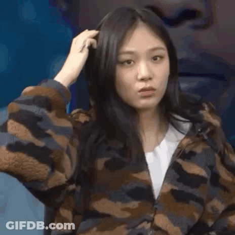 A Woman In A Camouflage Jacket Is Looking At The Camera While Holding Her Hair . GIF