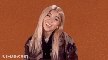 A Woman In A Camouflage Jacket Is Making A Funny Face And Giving A Thumbs Up . GIF
