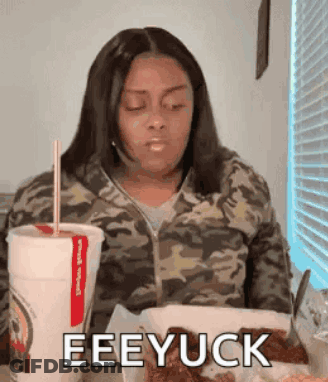 A Woman In A Camouflage Jacket Is Sitting At A Table Eating Chicken And Drinking A Cup Of Soda . GIF