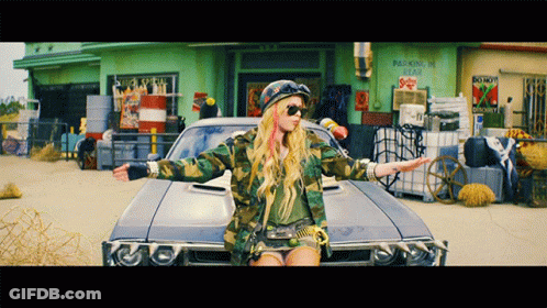 A Woman In A Camouflage Jacket Is Standing Next To A Car In Front Of A Building That Says Parking Is Illegal GIF