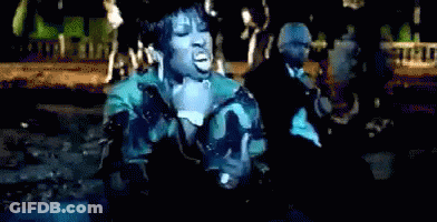 A Woman In A Camouflage Jacket Sings Into A Microphone In Front Of A Man In A Suit GIF