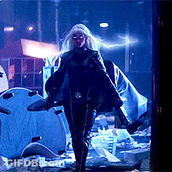 A Woman In A Cape Is Standing In A Dark Room With A Lightning Bolt Behind Her GIF